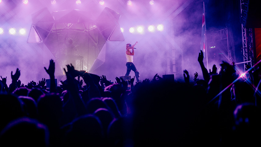 Musician Ski Aggu on stage, in the foreground the audience with raised hands
